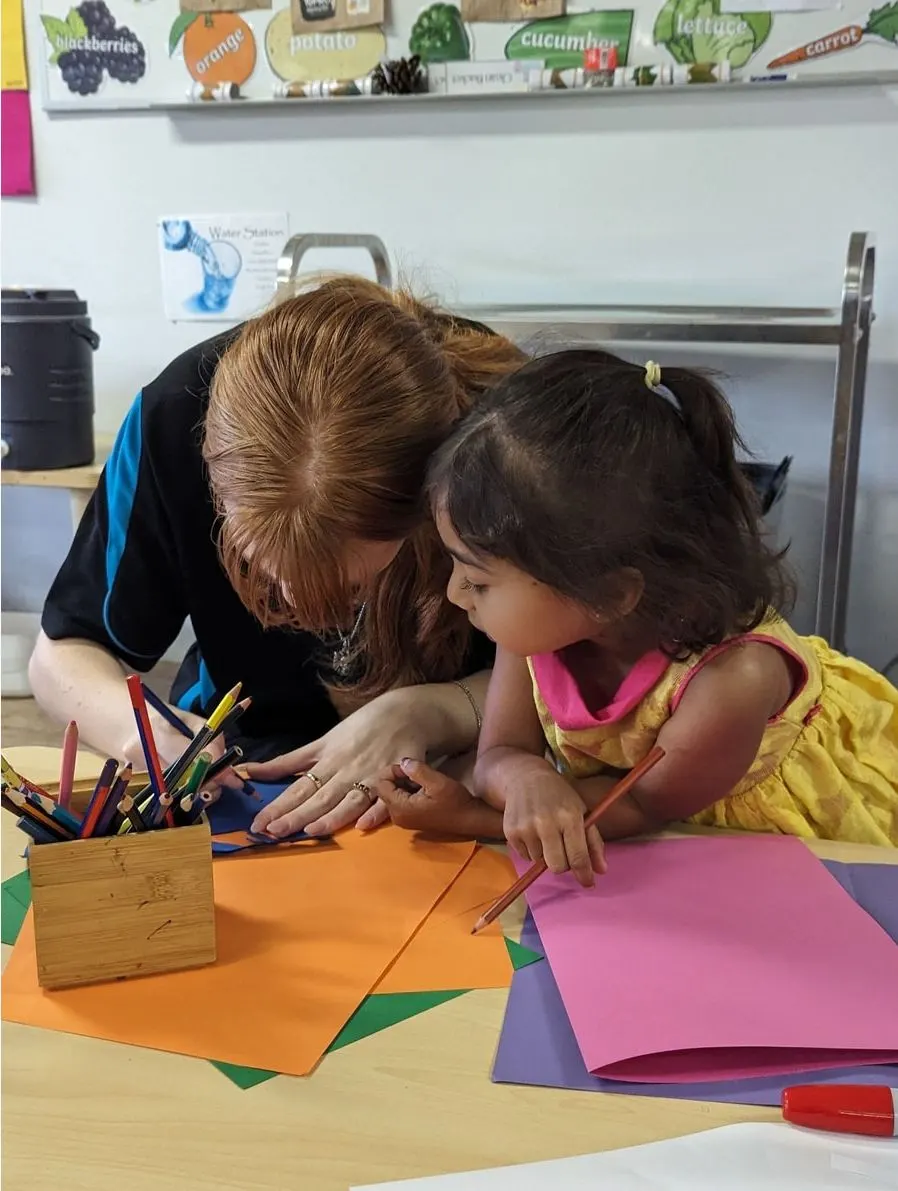 An educator drawing alongside a child at the craft table