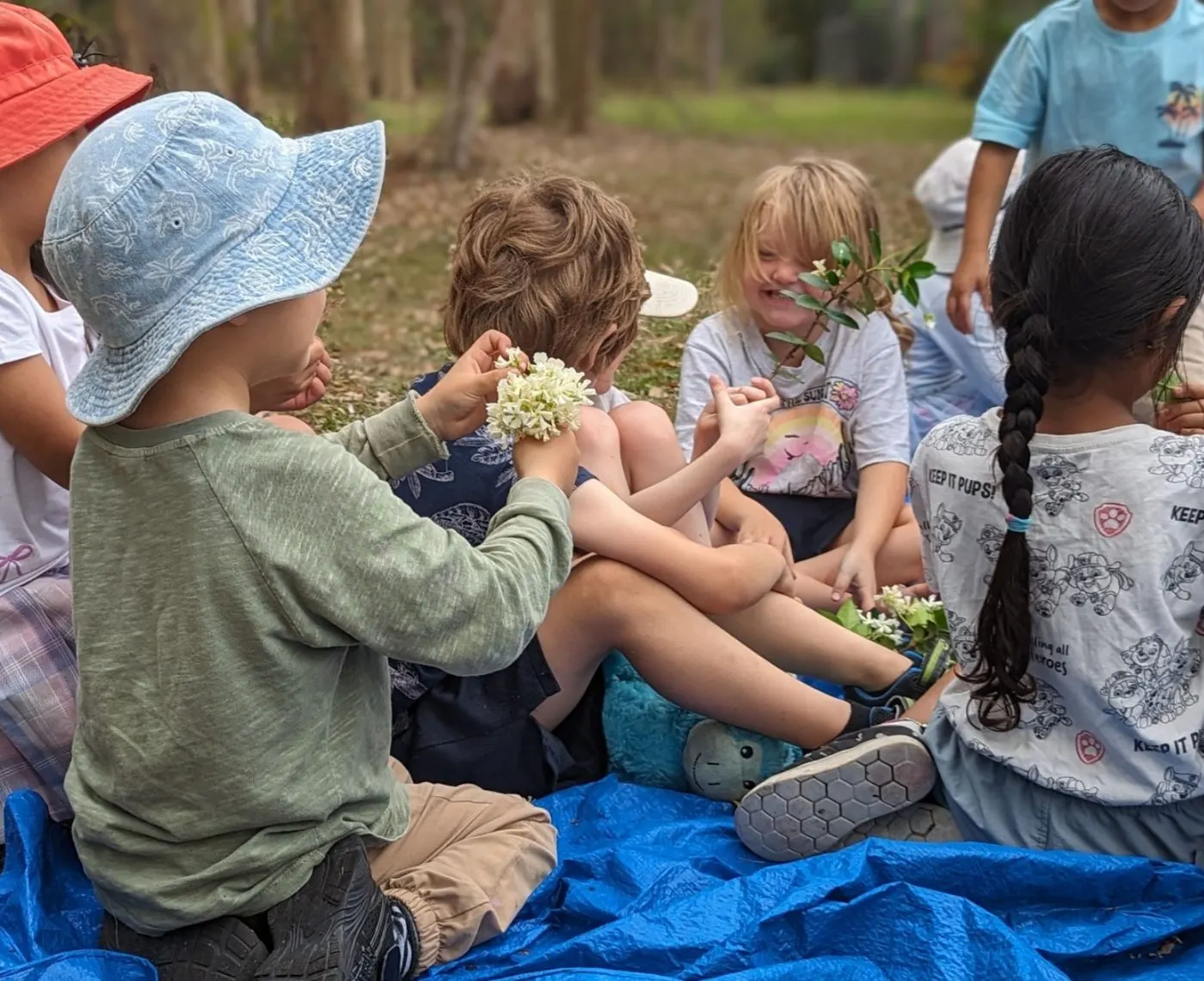 Children sitting on the picnic tarp looking at native flowers they have found
