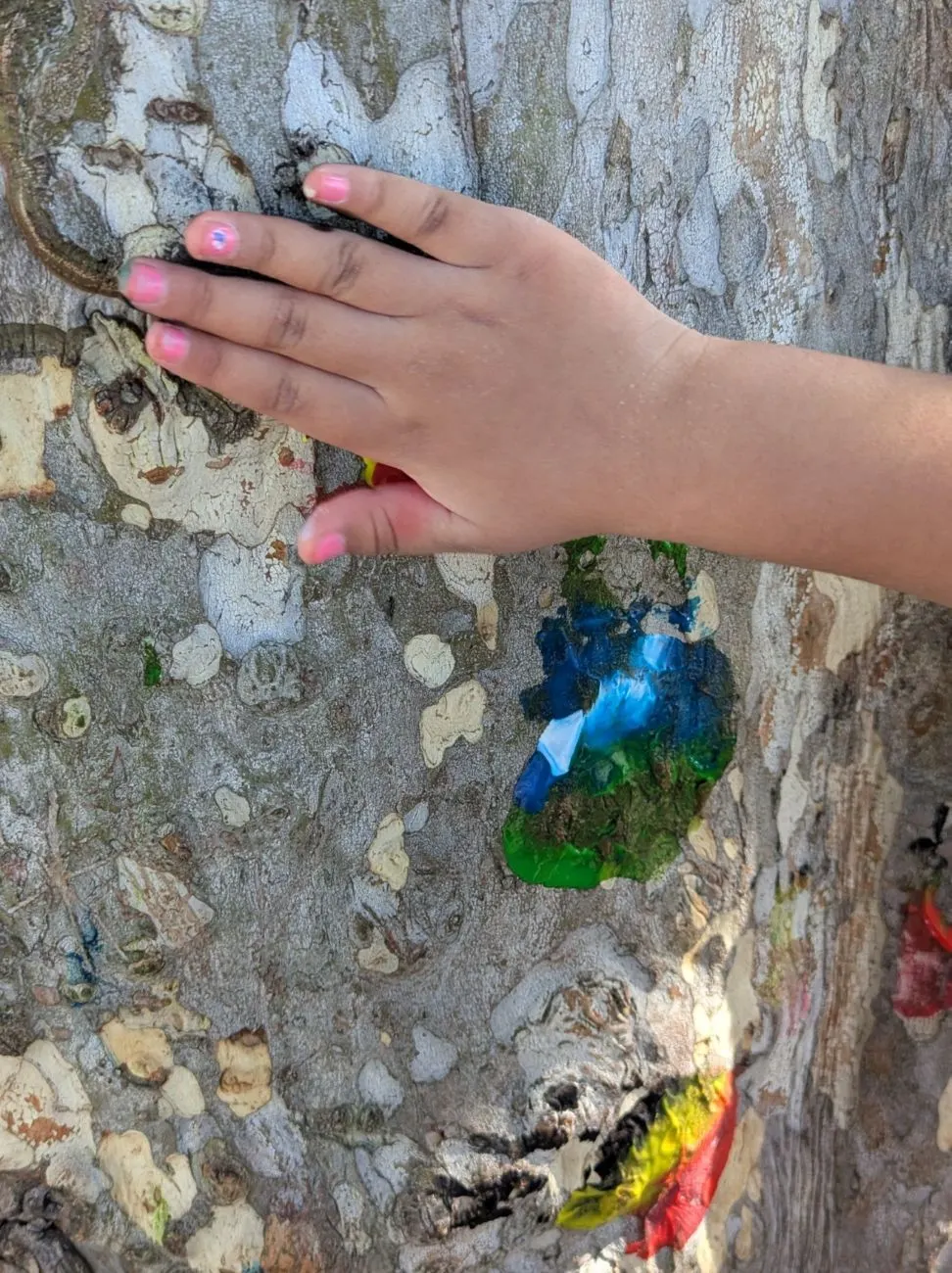 A child's hand resting on the bark of the painted tree