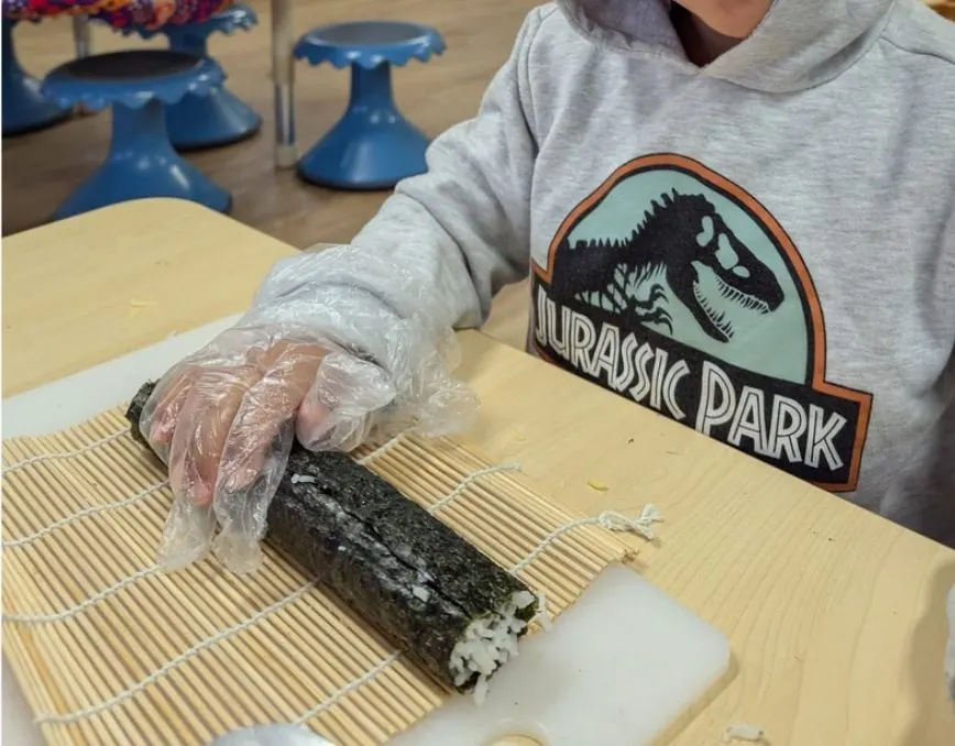 A child rolling sushi on a bamboo mat