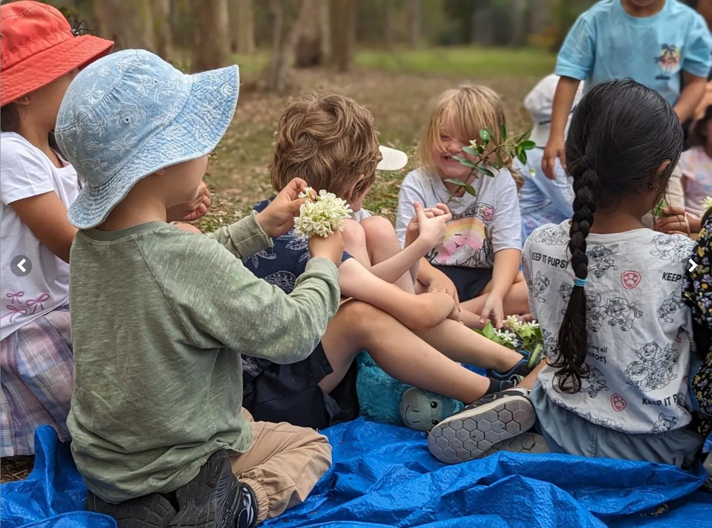 Children sitting together on the tarp at Bush Kindy, sharing the native flowers they have collected