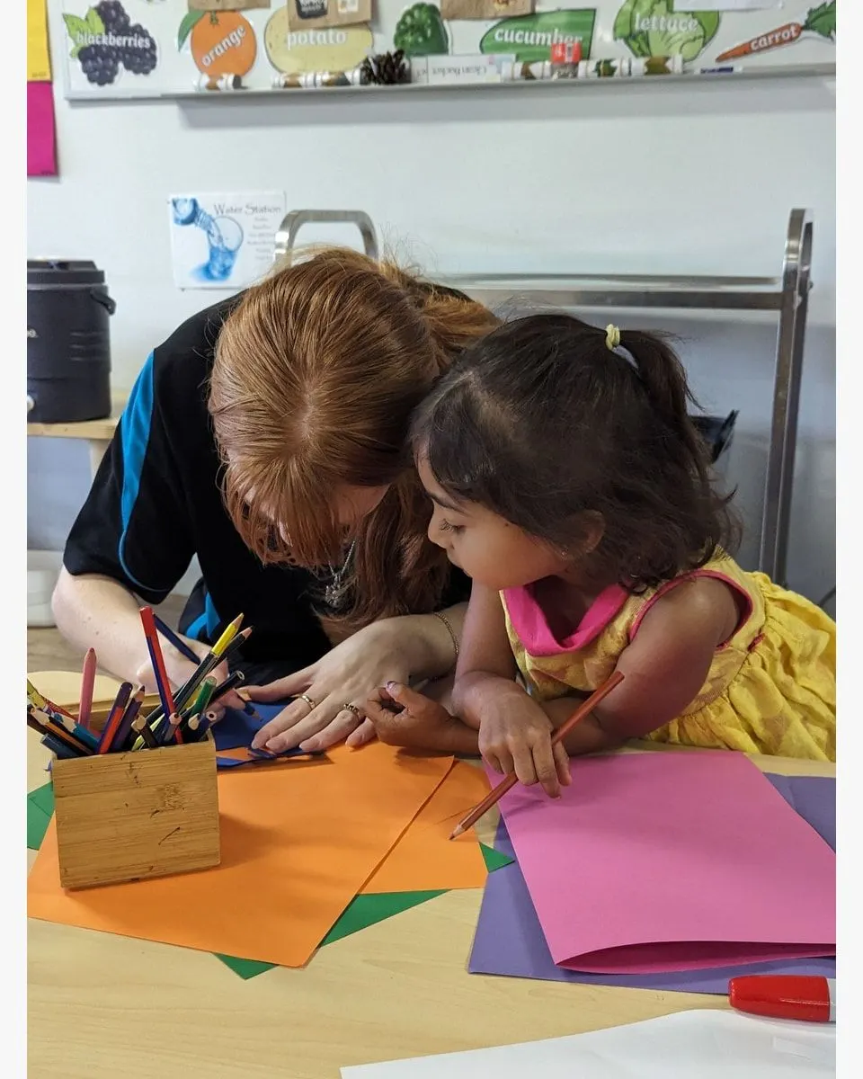 An educator drawing alongside a child at the craft table