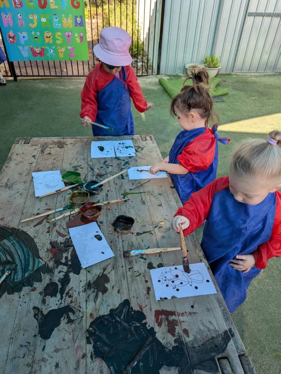 Children painting at the outdoor table in smocks