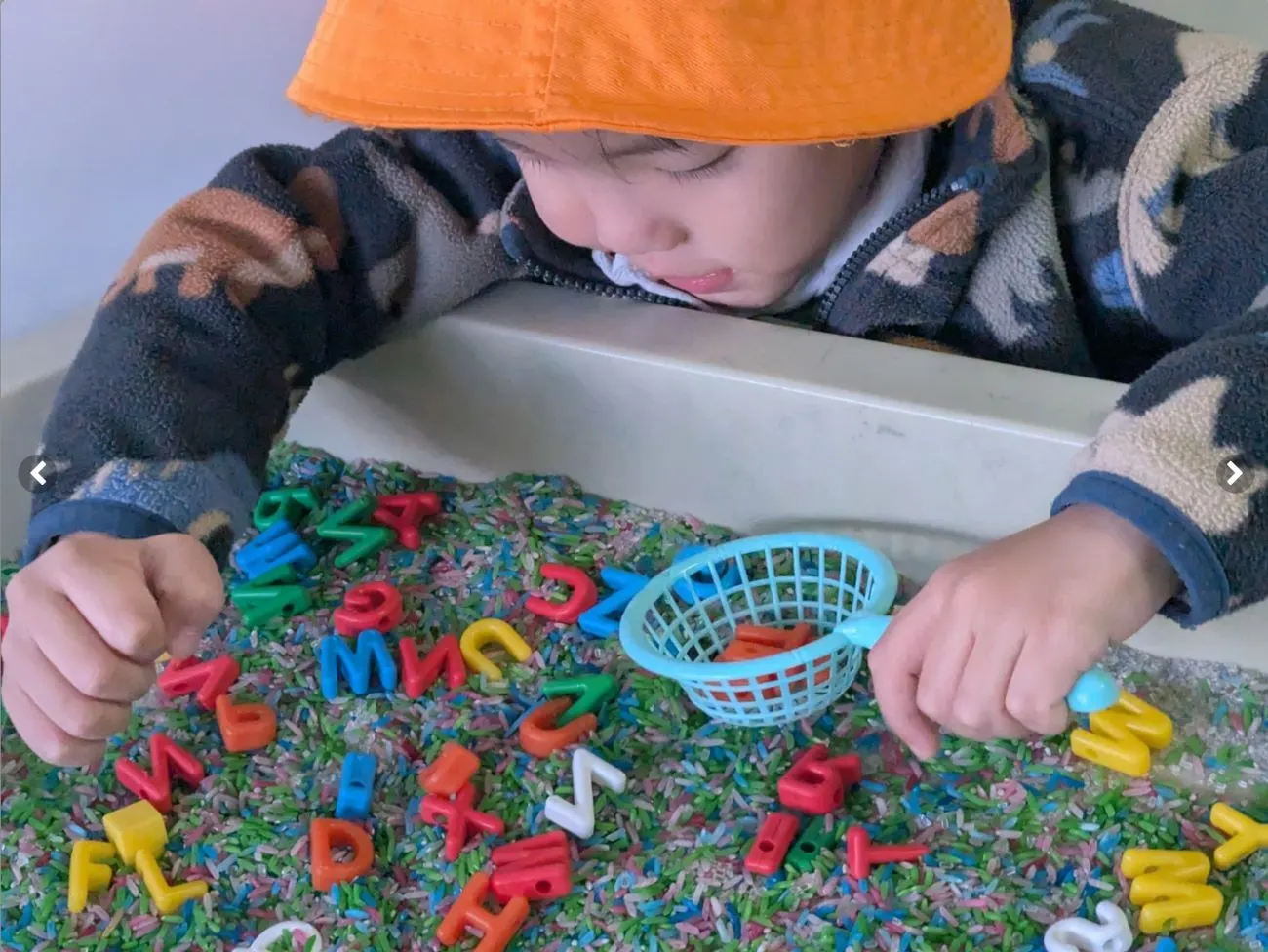 A child scooping letters out of a coloured rice sensory tray