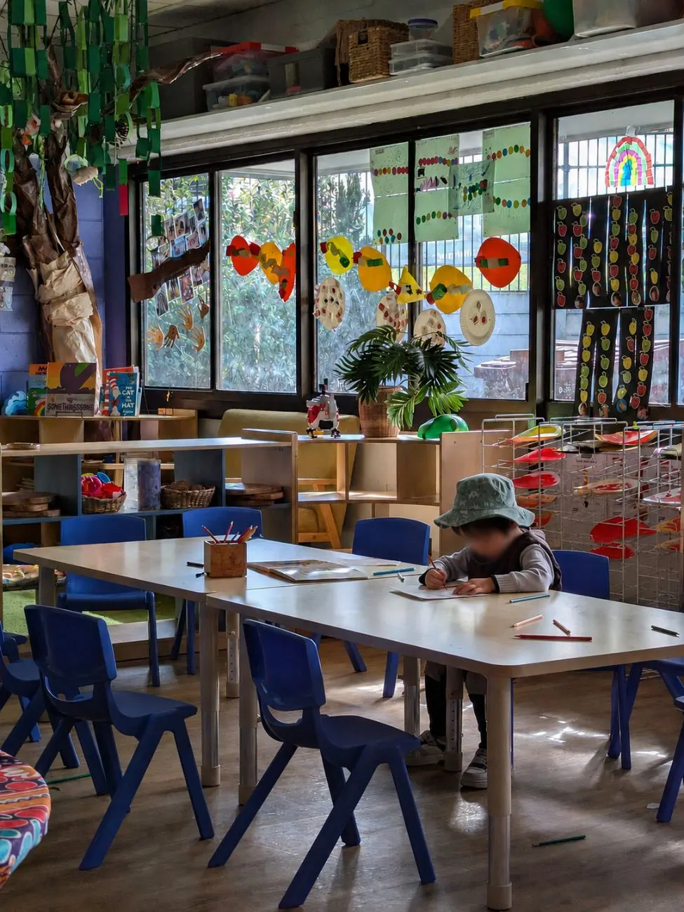 A child drawing at the project table beside the window