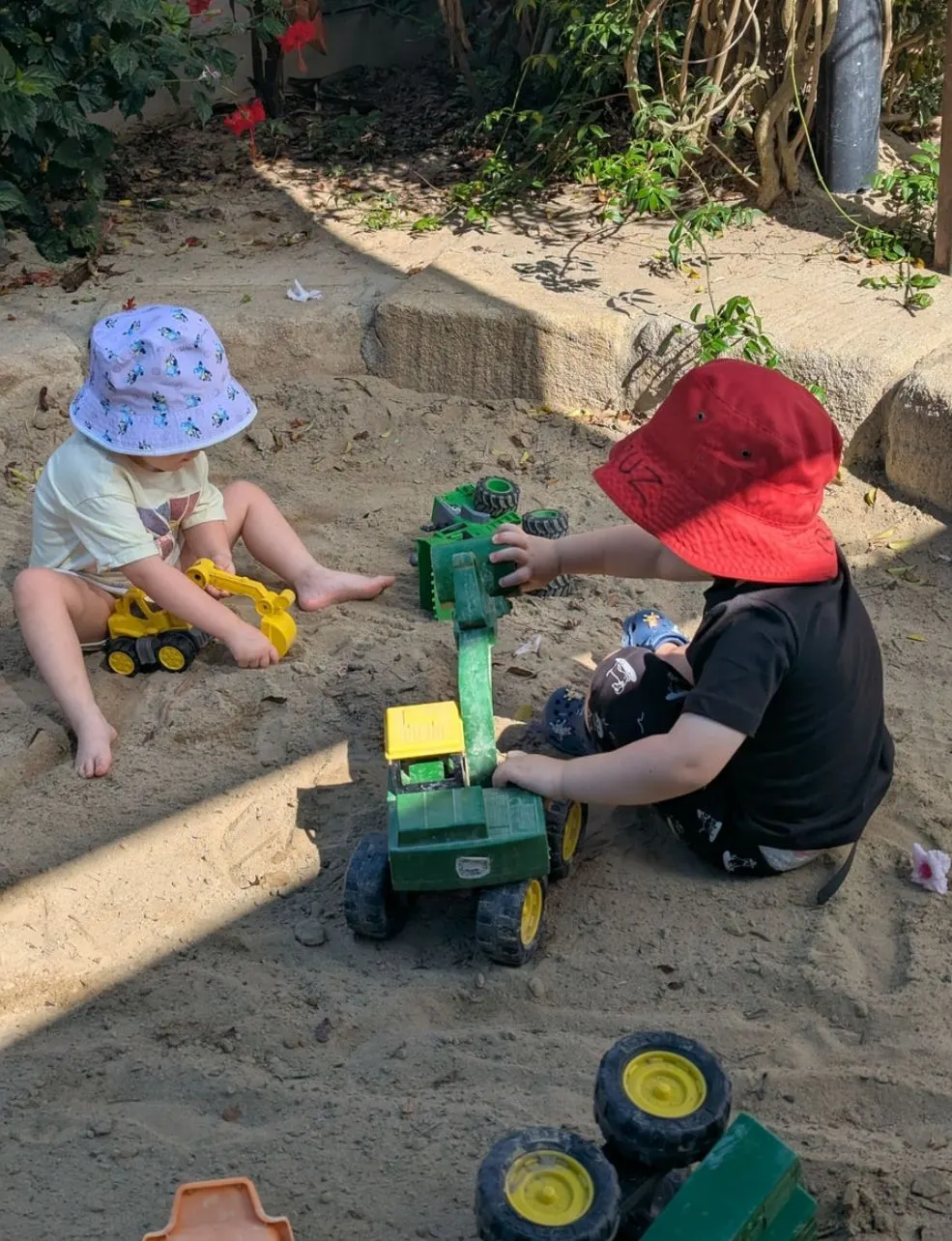Two children digging with diggers and trucks in the sandpit