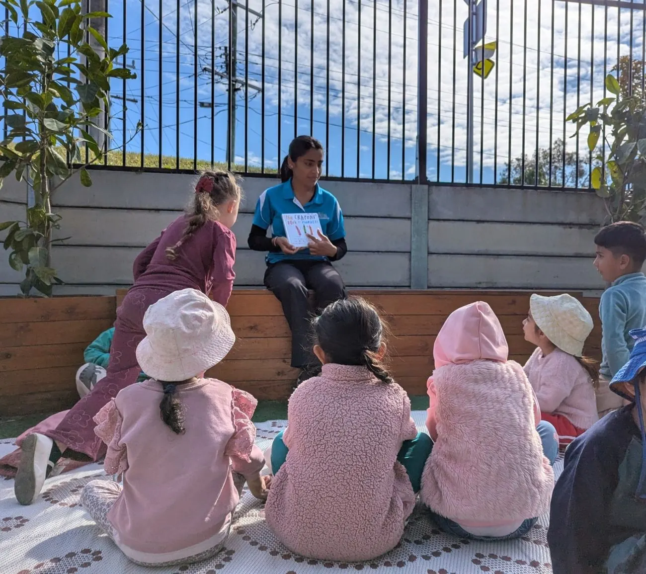 An educator reading a picture book to the group on the outdoor mat