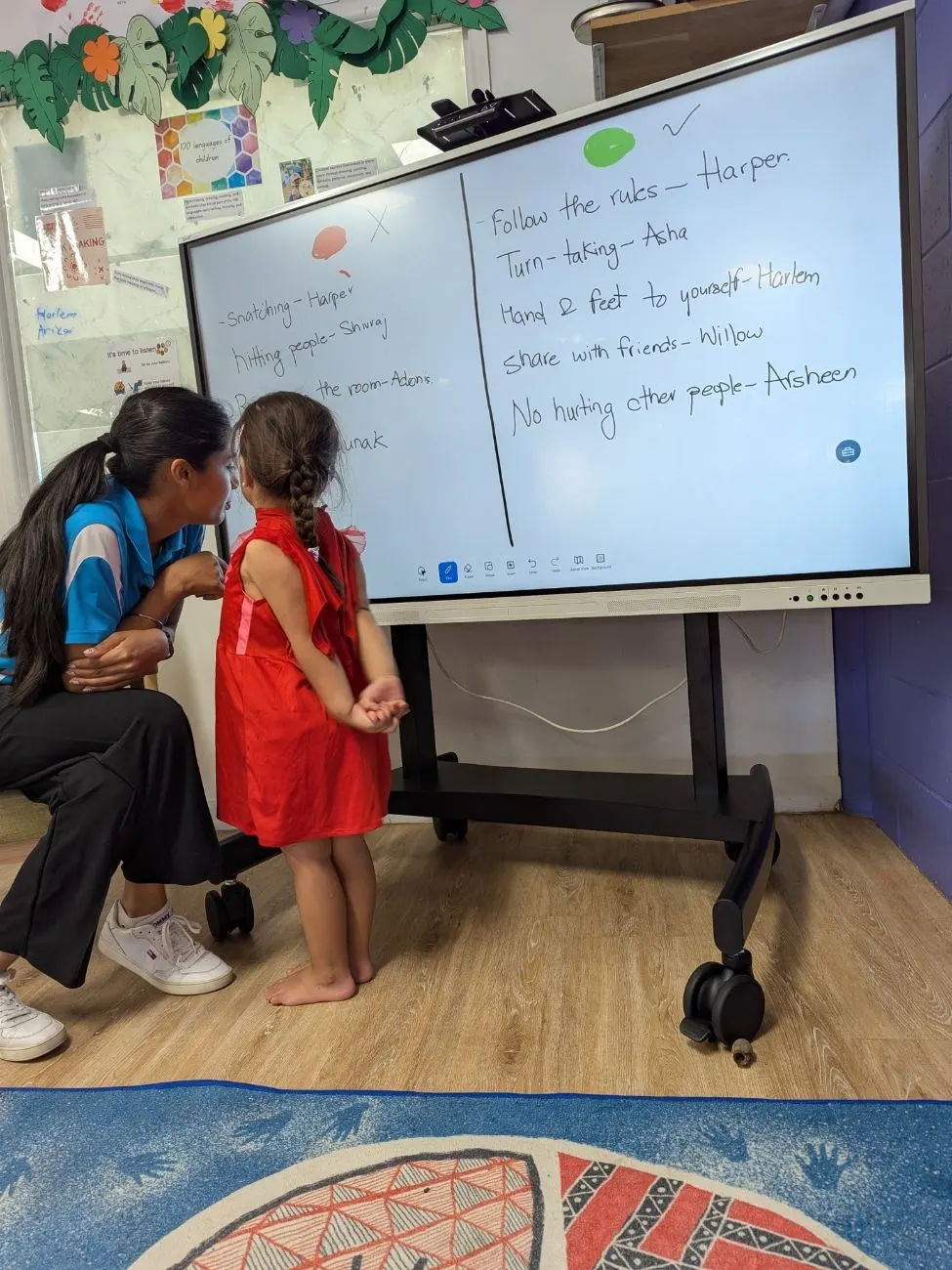 A child and educator at the board, writing the room's agreed rules together