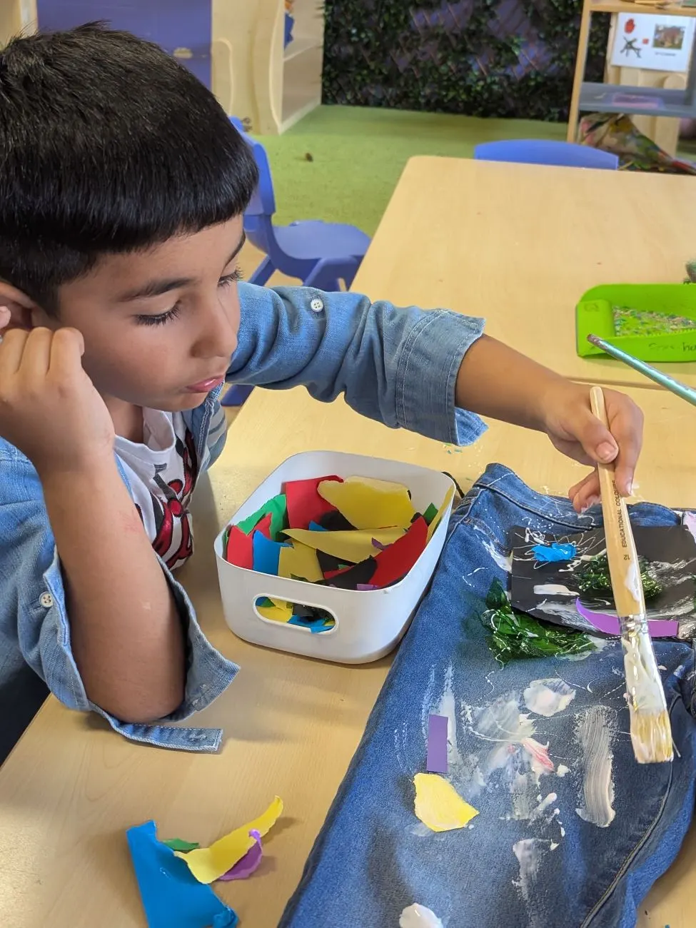A child gluing coloured paper onto a collage at the table