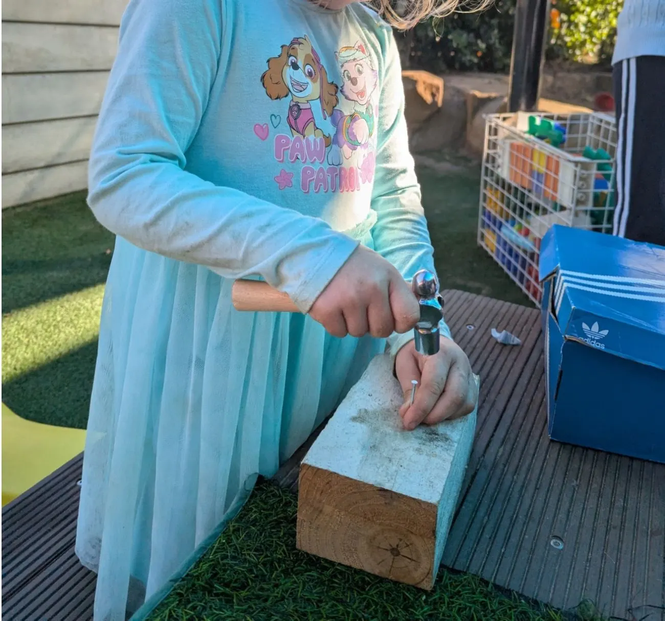 A child hammering a nail into a block of timber at the woodwork bench