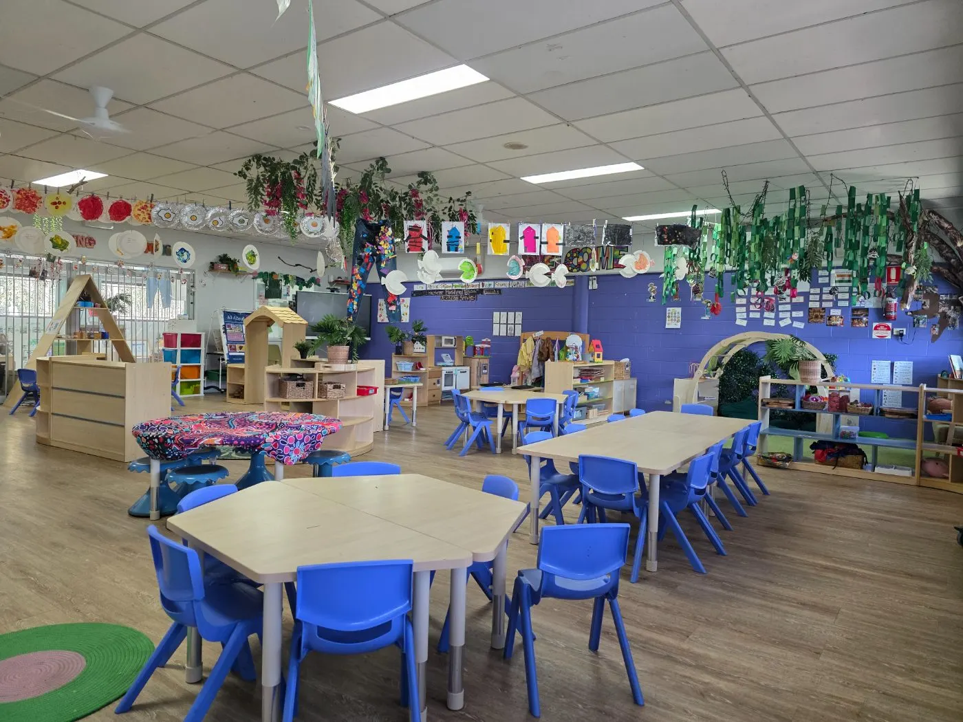 The Kindergarten room, with group tables, a mud-map play table and artwork hanging from the ceiling