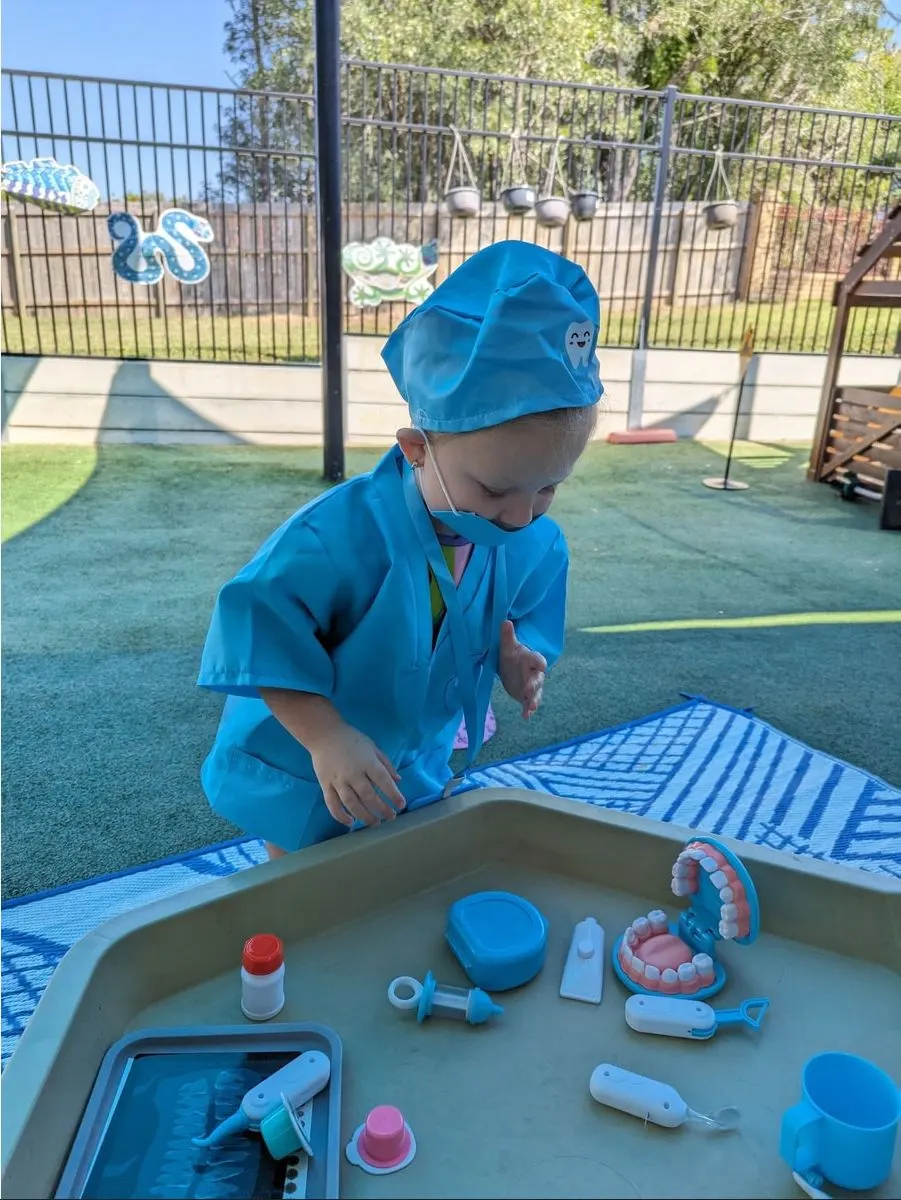 A child dressed as a dentist checking a doll at the outdoor tray