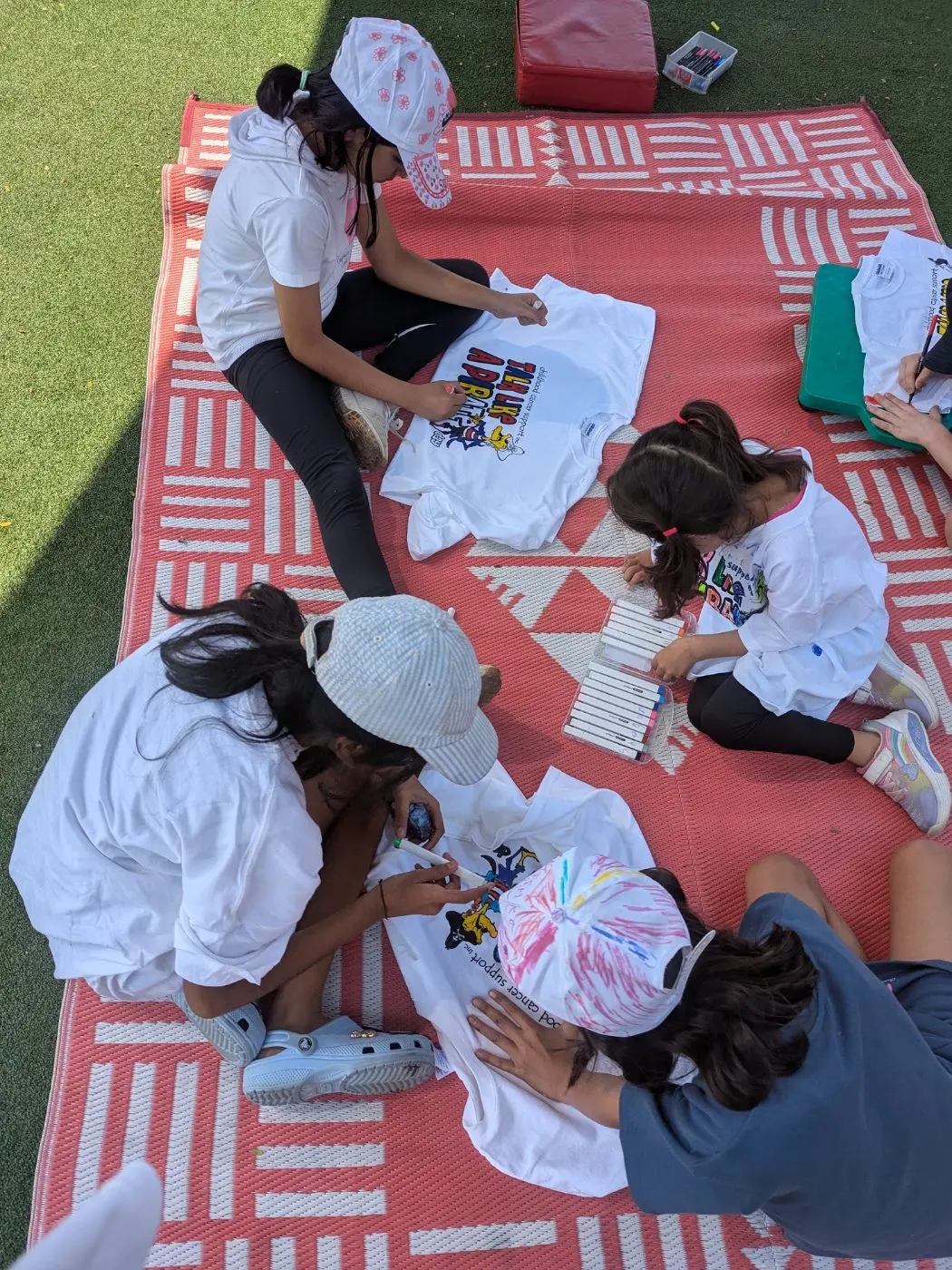 Children decorating t-shirts and caps with markers on a picnic rug