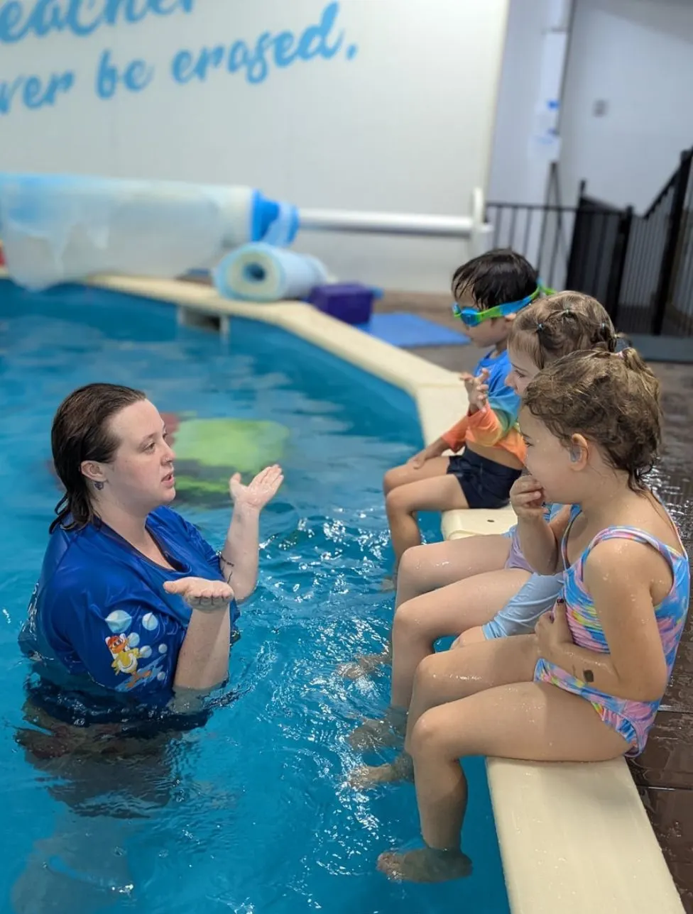 Children sitting on the pool edge listening to their swim teacher