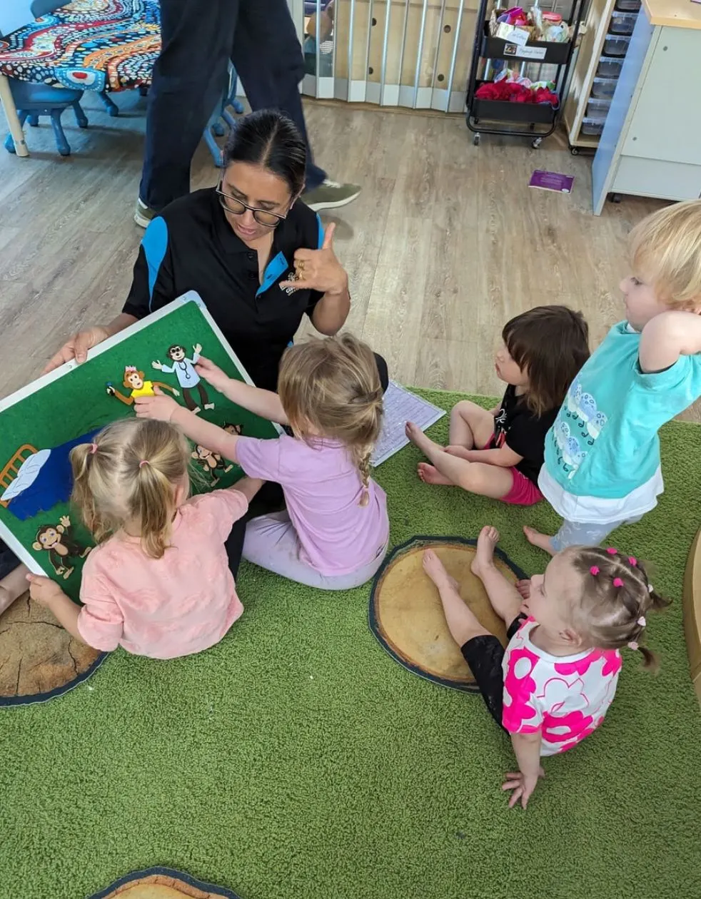 An educator telling a felt board story to a group of toddlers on the mat