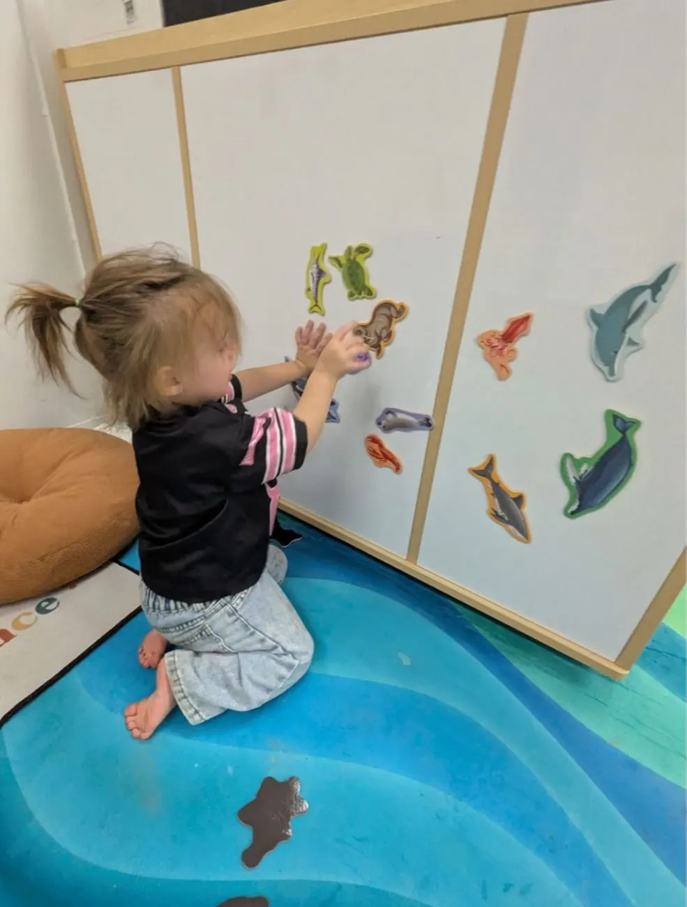 A toddler arranging sea creature magnets on a whiteboard