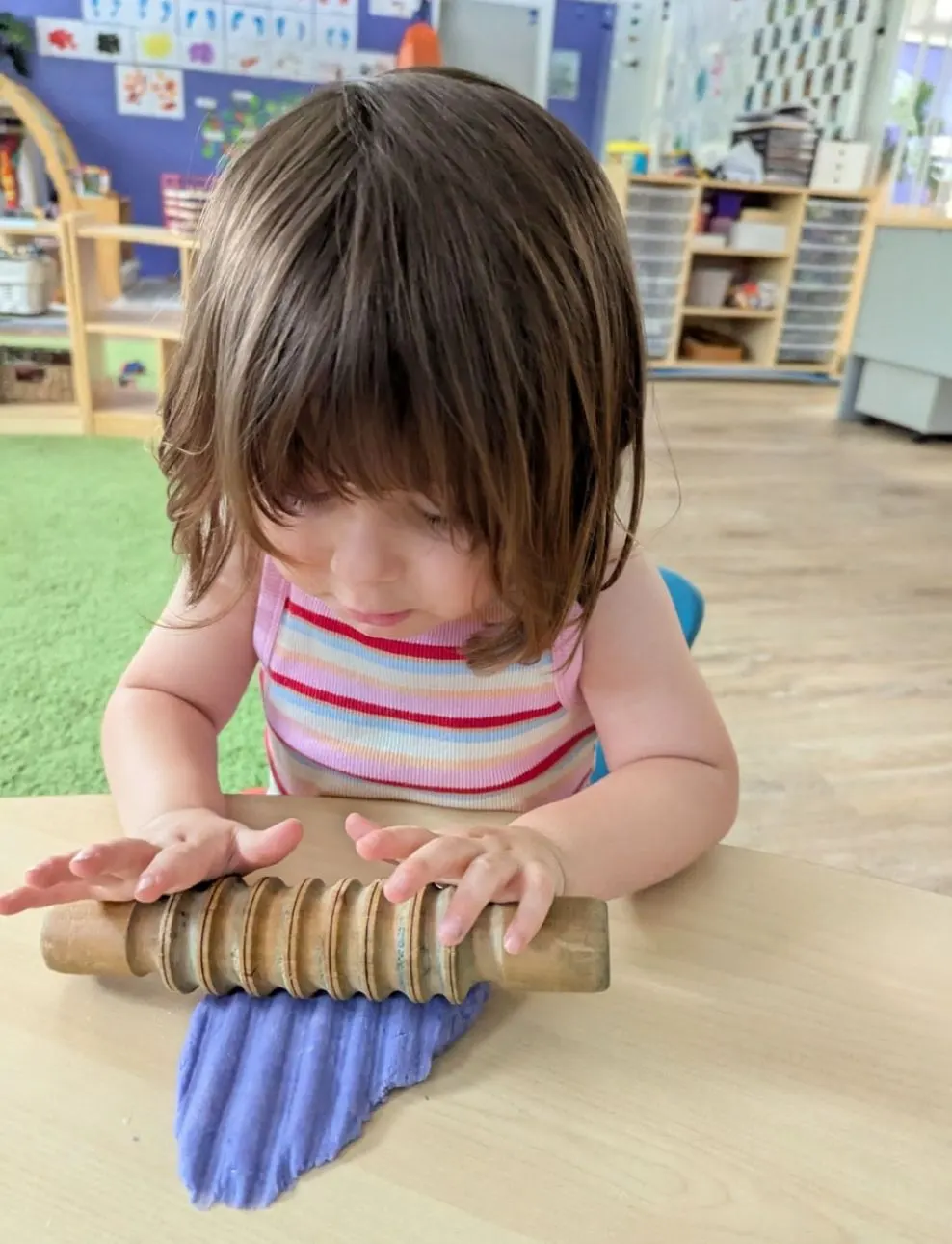 A toddler rolling playdough with a textured wooden roller