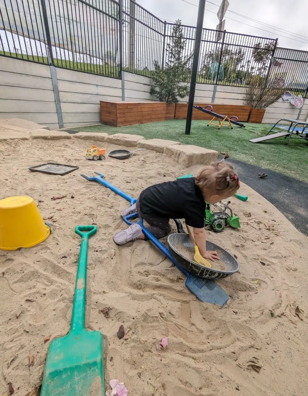 A toddler pushing a digger through the sandpit