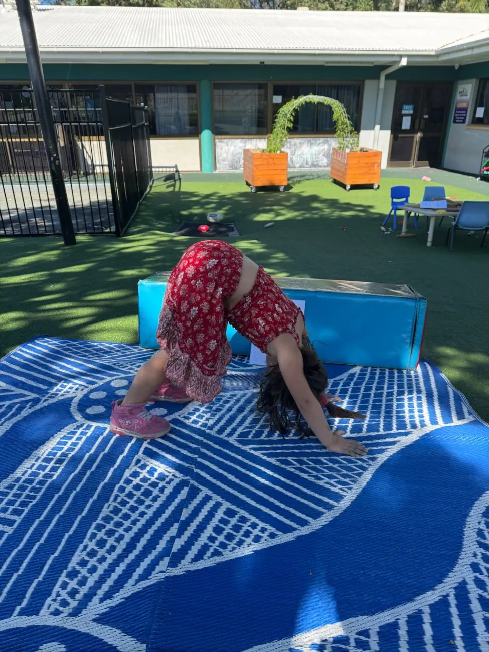 A child in downward dog on the yoga mat outside